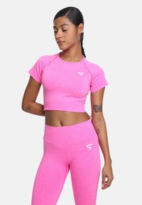 Ružičasti krojeni atletski top s kratkim rukavima i logom, uparen s ružičastim tajicama visokog struka. Tkanina izgleda rastezljivo i teksturirano.