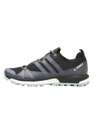 Chaussure de trail Adidas Terrex noire et grise avec semelle texturée et amorti blanc, vue latérale sur fond blanc.