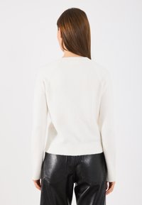 Biely pletený sveter s jemným lemovaním a manžetami, s jednoduchým okrúhlym výstrihom a mäkkou textúrou, skombinovaný s čiernymi koženými nohavicami.