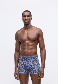 Kék boxer short, sötét levélmintával, rugalmas derékpánttal, amelyen "BJÖRN BORG" felirat található; puha, elasztikus anyagból készült a kényelem érdekében.