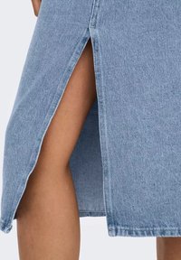 Světlá modrá džínová sukně s bočním rozparkem, zdobená třepícími se okraji a texturovaným povrchem. Tkanina vypadá pevná a ležérní.