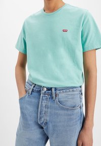 Mátově zelené bavlněné tričko s kulatým výstřihem a malým červeným logem Levi's na hrudi, spárované se světle modrými denními džíny.