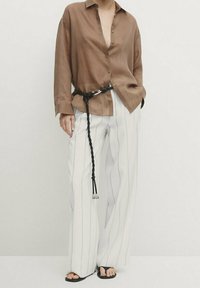 Chemise marron boutonnée avec une coupe décontractée, associée à un pantalon large à rayures blanches. Une ceinture noire tressée complète le look, avec des sandales plates.