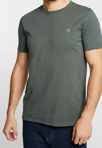 Kurzarm-T-Shirt mit Rundhalsausschnitt aus dunkelgrünem Baumwollstoff in taillierter Form. Verfügt über ein kleines gesticktes Logo auf der linken Seite.