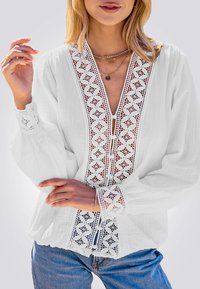 Witte blouse met lange mouwen, kantdetails bij de halslijn en manchetten, met een knoopsluiting en een gestructureerde stof. Gecombineerd met blauwe jeans.