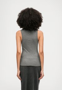Siva brezrokavnik z oprijetim dizajnom. Mehak, teksturiran material z visokim ovratnikom in subtilnim detajlom na hrbtu. V kombinaciji s temno krilom.