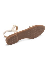 Złote sandały błyszczące z płaską podeszwą, regulowanym paskiem i teksturowaną brązową gumową podeszwą z kropkowanym gripem dla stabilności.