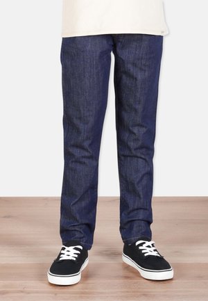 Slim-fit tummansiniset farkut, joissa on sileä rakenne, klassinen viiden taskun muotoilu ja jotka on yhdistetty mustiin lenkkareihin.