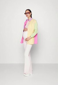 Camisa grande colorida em tons pastel de rosa, amarelo e verde, combinada com calças largas brancas e óculos de sol com lentes de tonalidade laranja.