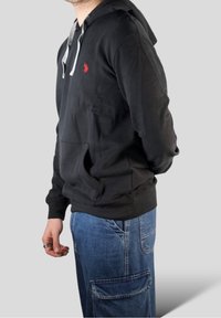 Czarna bluza z kapturem wyściełanym szarą podszewką, z przednimi kieszeniami i małym czerwonym logo. Do tego luźne niebieskie dżinsowe spodnie cargo z kieszeniami.