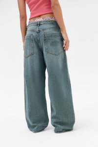 Helle, weit geschnittene Jeans mit einer strukturierten Oberfläche, ausgestattet mit einem Patches-Logo auf der Gesäßtasche und einem kontrastierenden blumigen Bund.