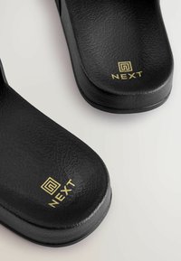 Infradito neri con superficie testurizzata, dotati di un logo dorato "NEXT" sulla soletta e una forma sagomata per il comfort.
