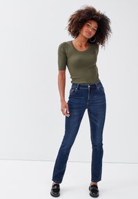 Olivfarbener, gerippter Kurzarm-Top kombiniert mit dunkelblauen High-Waist-Jeans, die ein klassisches Fünf-Taschen-Design und subtile Nähte aufweisen.