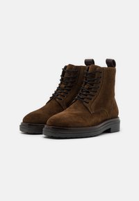 Brown suede ankle boots with black lace-up closure, padded collar, and a rugged black rubber sole. Features a loop tab at the back.