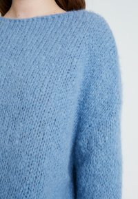 Ljusblå stickad tröja med lös passform, texturerat tyg med mjukt utseende och vid halsringning.