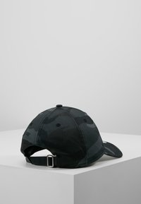 Camouflage baseball cap in shades of black and gray, made from textile material, featuring a curved visor and adjustable strap at the back.