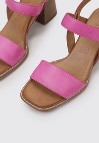 Les sandales en cuir rose disposent de deux larges brides, d'un talon bloc en bois texturé et d'une semelle en cuir beige cousue.