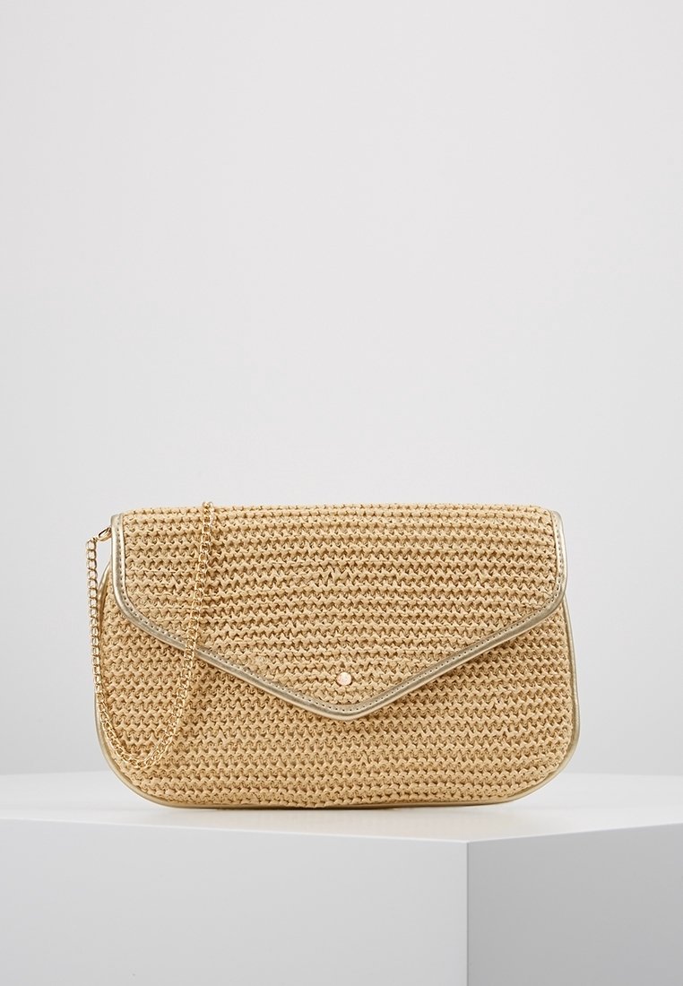 Ratanová taška v béžové barvě s víkem, kovovým lemováním a řetízkovým popruhem. Na přední straně je malý kovový hřebík jako detail.