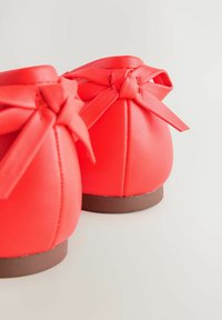 Rote Lederschuhe mit einer glatten Textur, abgerundeter Form, kurzen Absätzen und zwei gebundenen Schleifen auf der Rückseite. Sichtbare braune Sohle.