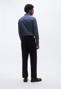 Tamsiai mėlyna marškiniai su tekstūruotu audiniu, derinami su tamsiomis kelnėmis ir rudos spalvos batais. Demonstracija paprasto, pritaikyto dizaino.