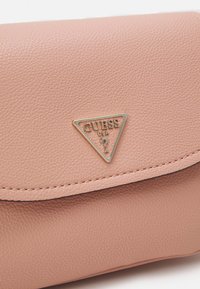 Růžová strukturovaná syntetická kožená peněženka se zlatým trojúhelníkovým logem Guess USA na přední straně, která disponuje klopovým uzávěrem a prošívanými detaily.