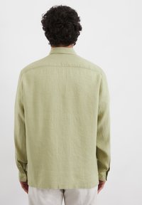 Chemise à manches longues vert clair en tissu texturé, avec un col, des poignets à boutons et une coupe droite. Aucune motif ni graphique présent.