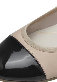 Gros plan d'une chaussure plate beige avec un bout en cuir verni noir brillant et une doublure rembourrée au niveau du col.