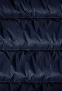 Marineblauwe pufferjas van stof, doorstikt met horizontale naden, met een gladde, glanzende textuur en een subtiel lijnpatroon.