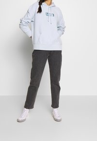 Sudadera con capucha azul claro con un bolsillo frontal, con el logo de Levi's. Combinada con jeans grises de tiro recto y zapatillas blancas de caña alta.