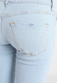 Vaqueros de mezclilla azul claro con un diseño ajustado, que cuentan con bolsillos traseros curvados con costuras en contraste y un sutil acento en forma de triángulo sobre un bolsillo.