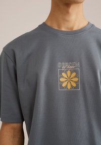 Gray cotton t-shirt featuring a printed graphic design with a yellow flower and "GARDEN of hope" text in contrasting colors.