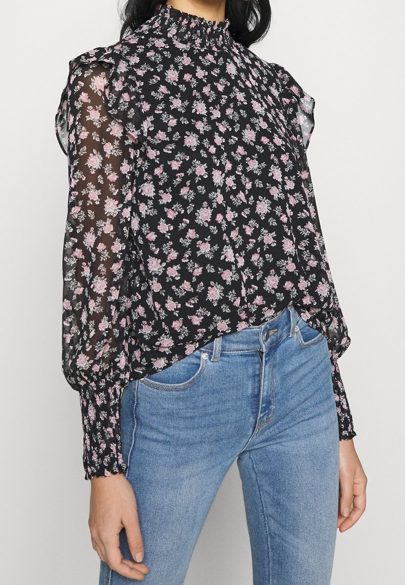 Black floral blouse with pink and white flowers, sheer sleeves, ruffled neckline, and elastic cuffs. Paired with light blue jeans.