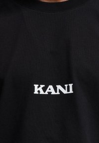 Black cotton t-shirt featuring a white printed logo "KANI" on the front. The material has a smooth texture with a crew neckline.