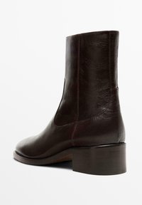 Hnědá kožená kotníková bota s hladkou texturou, zaoblenou špičkou a nízkým blokovým podpatkem. Obsahuje boční pružný díl pro snadné obouvání.