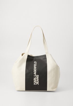 Canvas tote bag in cream and black, featuring a bold black stripe with "KARL LAGERFELD JEANS" printed vertically. Wide, sturdy handles.