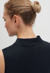 Marineblaues ärmelloses Kleid mit hohem Kragen, ausgestattet mit einem Reißverschluss im Rücken, aus einem glatten Stoff mit einer subtilen Textur.