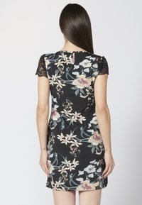 Elegantes schwarzes Blumenkleid mit kurzen Spitzenärmeln, das eine Vielzahl von Pastellblumen und ein Schlüsselaugen-Detail im Rücken für gestalterisches Interesse aufweist.