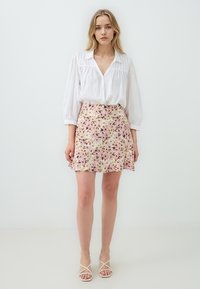Weißes Hemd mit Puffärmeln und einem A-Linien-Rock mit Blumenmuster in Pastellfarben. Der Rock hat einen ausgestellten Saum und eine weiche Textur.