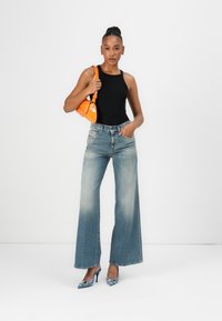 Black sleeveless top, light blue wide-leg jeans with fading, blue pointy heels, and an orange handbag with a curved design.