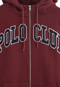 Mörkröd zip-up hoodie i bomullsblandning, med en stor broderad "POLO CLUB" i vitt och marinblått, samt matchande dragskor och framfickor.