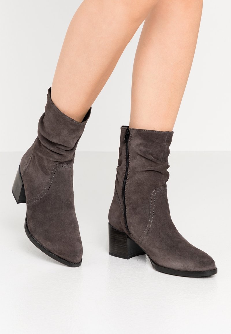 Bottines en suède gris avec un design légèrement décontracté, bout pointu et un talon bloc de hauteur moyenne. Fermeture éclair sur le côté pour un enfilage facile.