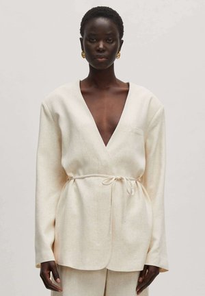 Cream-colored wrap top with a deep V-neck, long sleeves, and a tie waist. Made from a lightweight, textured fabric.
