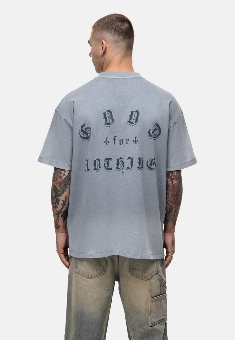 Szara, oversize koszulka z krótkim rękawem i okrągłym dekoltem, z czarnym nadrukiem na plecach, wykorzystującym różne czcionki. Casualowy styl.