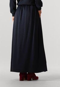 Marineblauwe maxi rok met een elastische tailleband, met een gladde, vloeiende textuur en zijzakken. Gecombineerd met rode enkellaarzen.