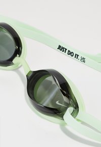 Hellgrüne Schwimmbrille mit dunklen, getönten Gläsern, Nike-Logo auf einem Glas und dem Text "JUST DO IT." auf dem Band.