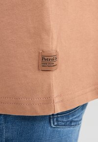 Camisa de manga corta color durazno claro, hecha de algodón suave, con una pequeña etiqueta marrón que dice "Petrol Inc." cosida en el dobladillo.