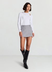 White ribbed cardigan with button closures, paired with a gray mini skirt featuring pockets, and black knee-high heeled boots.