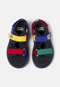 Kleurrijke kindersandalen van zacht, textuurmateriaal; voorzien van verstelbare banden in rood, geel, groen en blauw, met een rubberen zool.