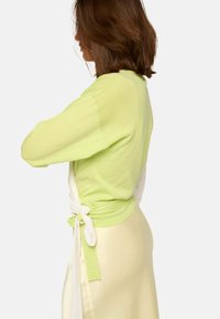 Pull long à manches longues vert clair avec un dos blanc, noué à la taille. Texture douce, coupe décontractée, complété par une jupe jaune pâle.
