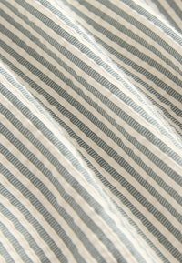 Tela de algodón con franjas delgadas alternadas en blanco roto y azul apagado, que presenta una textura sutil y una apariencia ondulada.